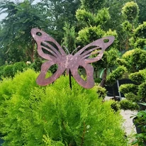 Ornamentul de grădină din metal, în formă de fluture mare, pare să se așeze cu grație pe plantă.